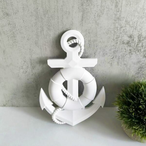 White decorative anchor sculpture with coiled rope, placed on a light gray wall beside a small green plant.