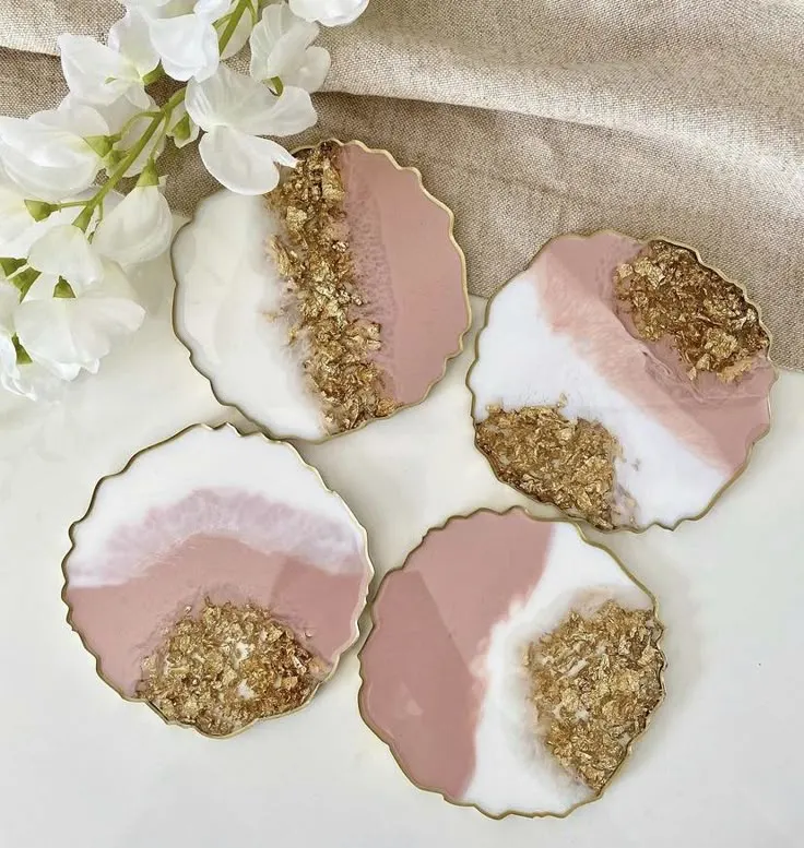 Set of four scalloped-edged coasters featuring pink, white, and gold leaf geode designs on a light surface with white flowers nearby.