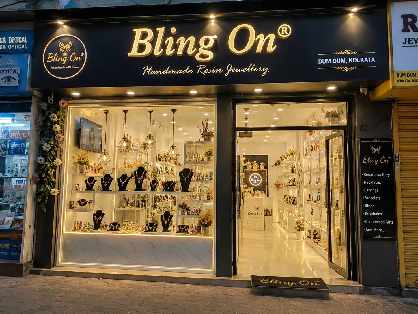 Front of Bling On, a handmade resin jewellery shop, with glass display windows full of necklaces and earrings in view. Exterior of Bling On store at night with glowing sign and showroom filled with jewelry displays. Shop window displays jewelry on black busts and shelves, entrance to Bling On. Boutique storefront for Bling On Resin Jewellery, with bright interior lighting and products arranged on shelves. Doorway into Bling On jewellery store, gold-toned sign, mannequins with necklaces behind glass.